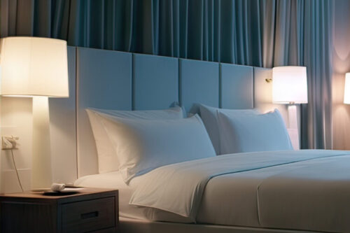 Ein modernes, stilvoll beleuchtetes Hotelzimmer mit großem Bett, Sitzbereich und bodentiefem Fenster mit nächtlicher Stadtansicht.